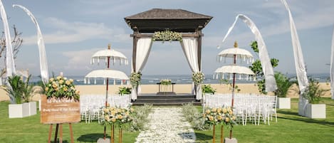 Decoración para una boda en la playa, con un arco de madera, cortinas blancas y arreglos florales.