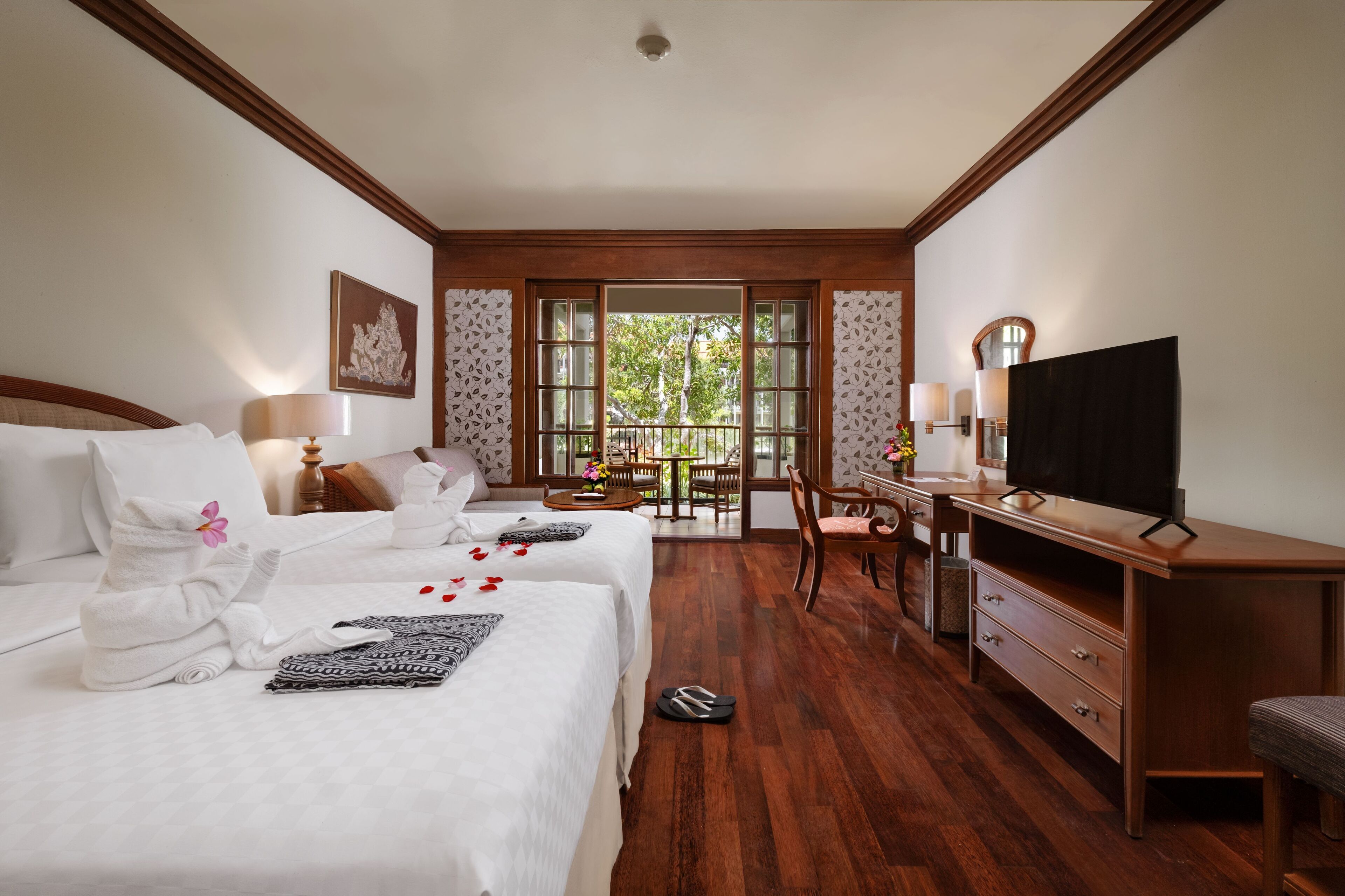 Una habitación de hotel con dos camas, un escritorio, una televisión y un balcón con vistas a árboles.