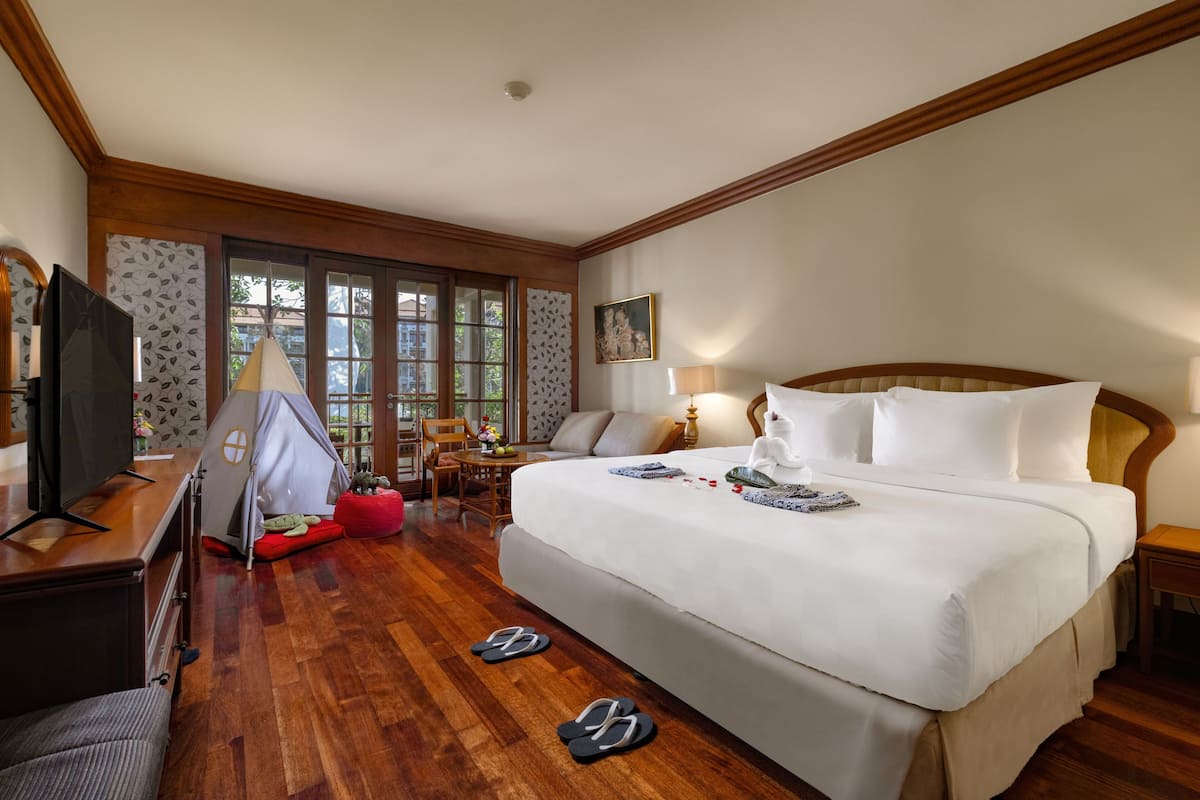 Une chambre d’hôtel avec un grand lit, une télévision, une tente et une fenêtre donnant sur la forêt.