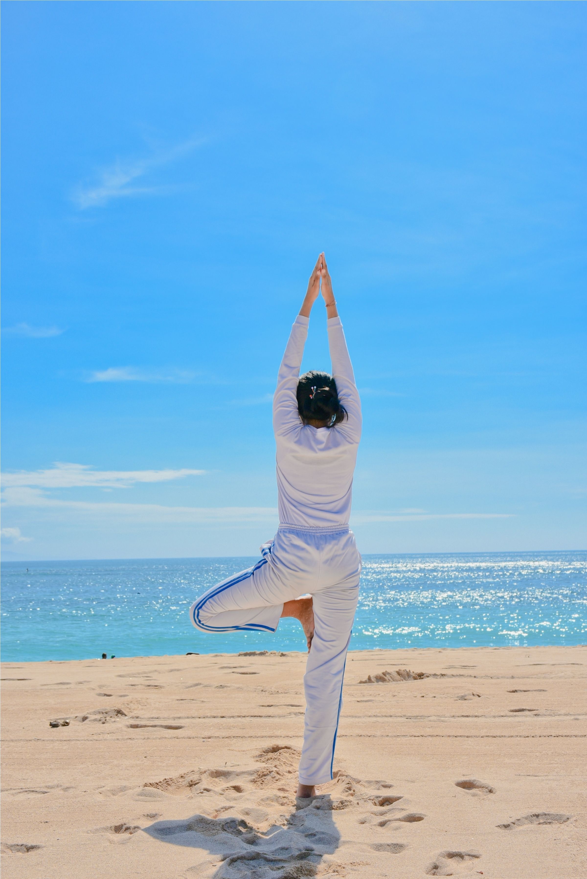 Uma pessoa fazendo uma pose de yoga numa praia, com um céu claro e oceano ao fundo.