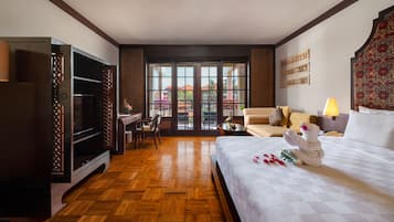 A hotel room with a large bed, a desk, a TV, and a balcony with a view of buildings.