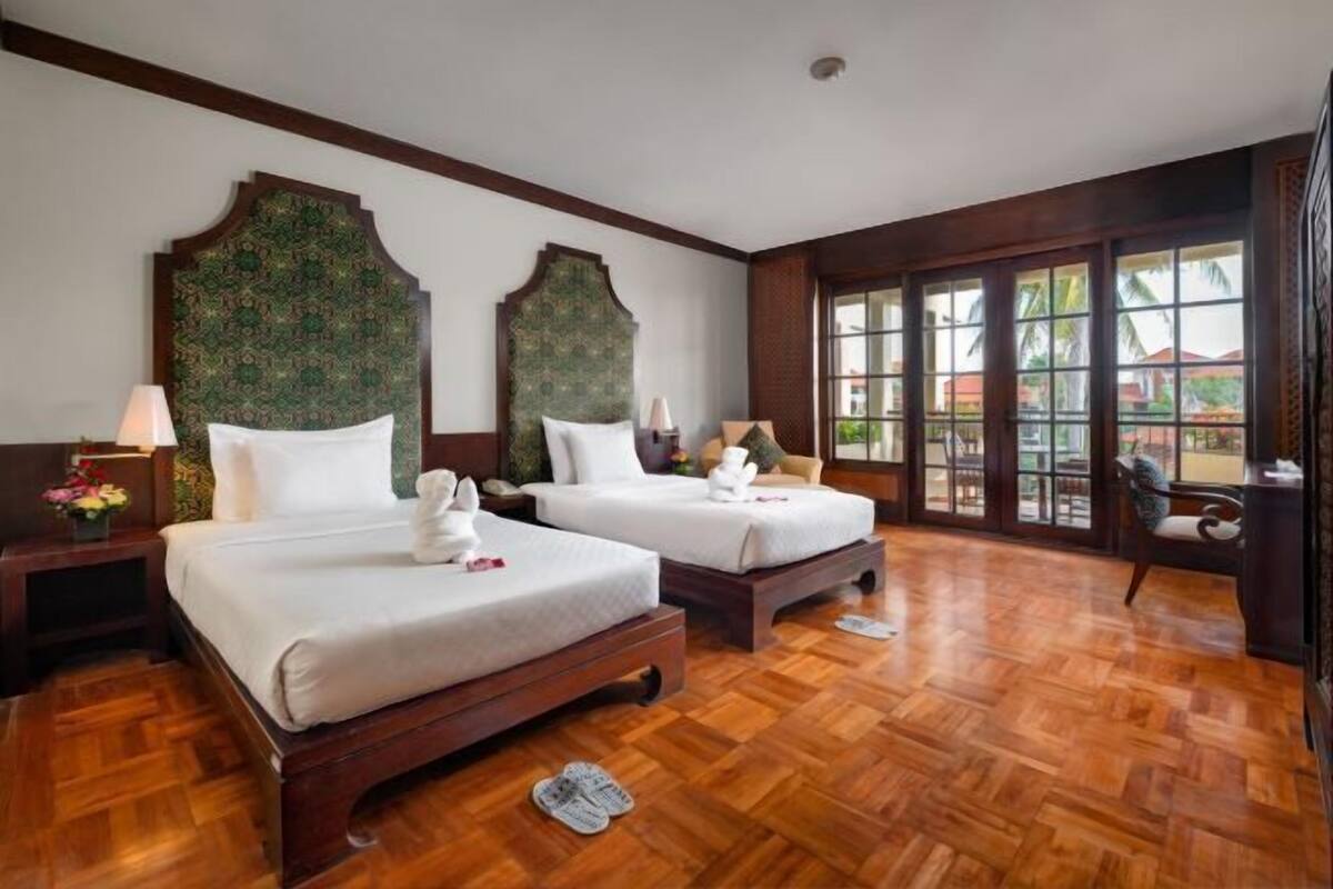 Une chambre d’hôtel avec deux lits, un plancher en bois, de grandes fenêtres et une vue sur l’extérieur.