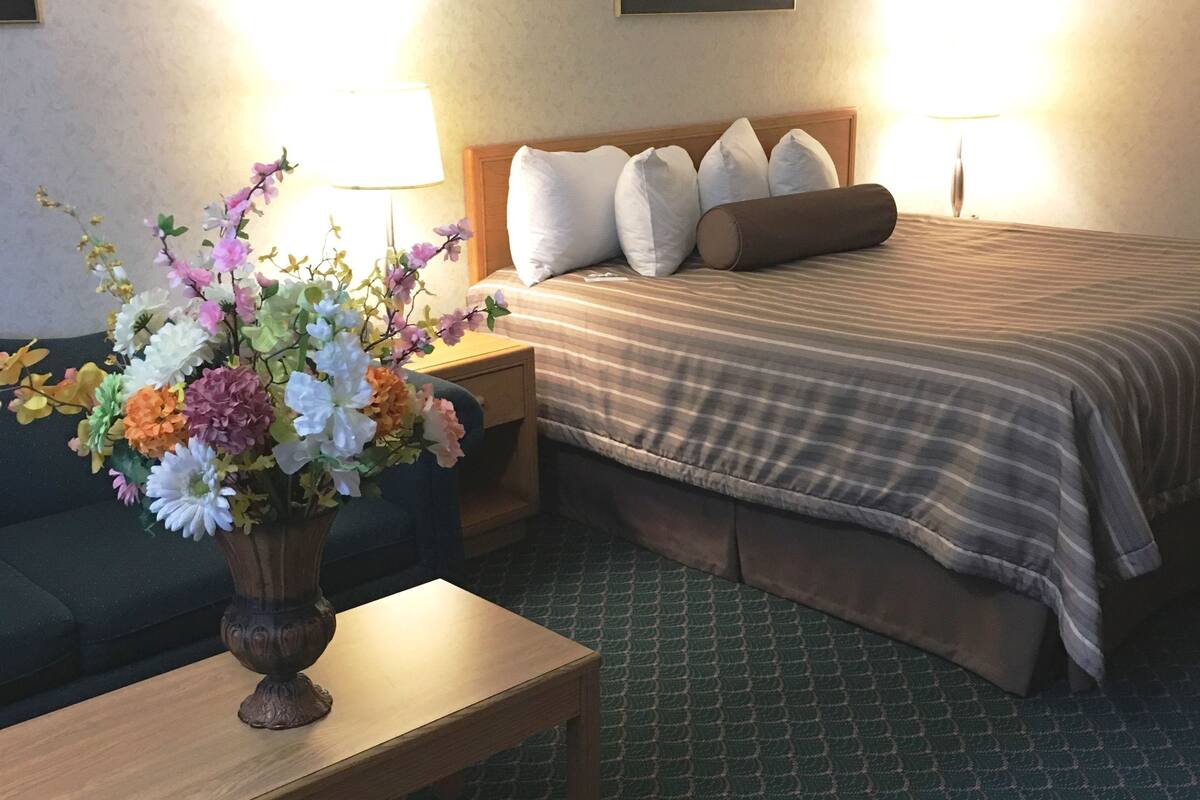 A hotel room with a bed, a nightstand, a lamp, a vase of flowers, and a green patterned carpet.