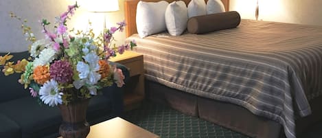 A hotel room with a bed, a nightstand, a lamp, a vase of flowers, and a green patterned carpet.