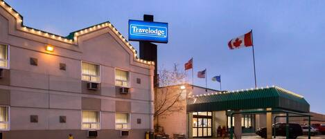Un hotel Travelodge con un letrero, un estacionamiento y una bandera.