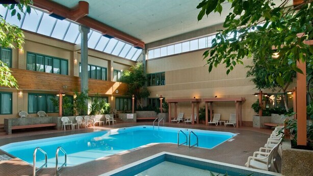 Piscina interior con varias pistas, rodeada de sillas de descanso y plantas en macetas.