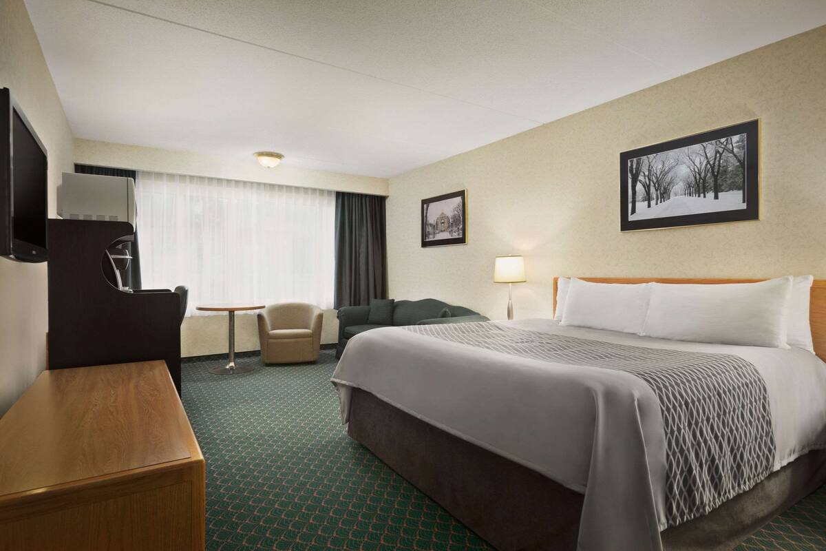 A hotel room with a bed, a desk, a chair, a TV, and a window with curtains.