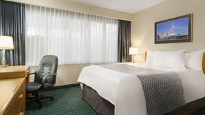 Habitación de hotel con cama, escritorio, silla y ventana con cortinas.