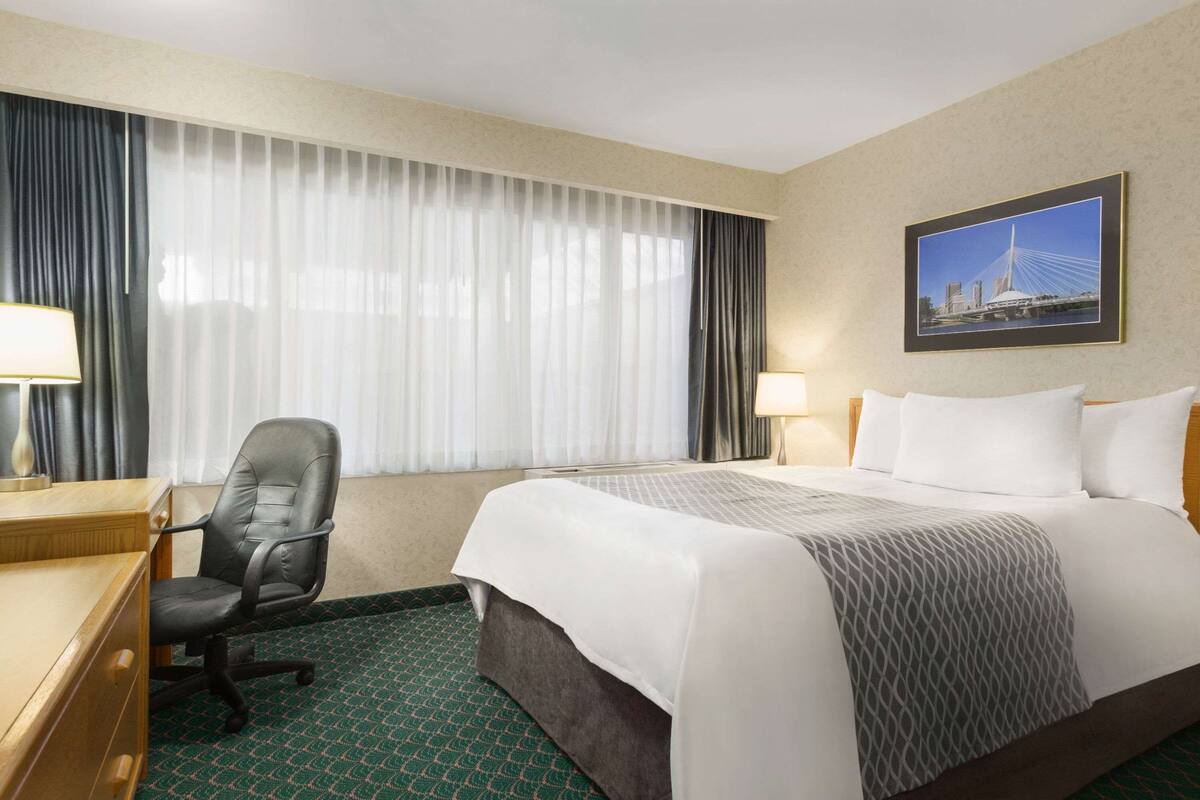 A hotel room with a bed, a desk, a chair, and a window with curtains.