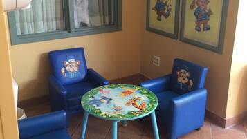 Relax in this cozy patio area with a table and two chairs, surrounded by framed artwork and a window with green curtains.