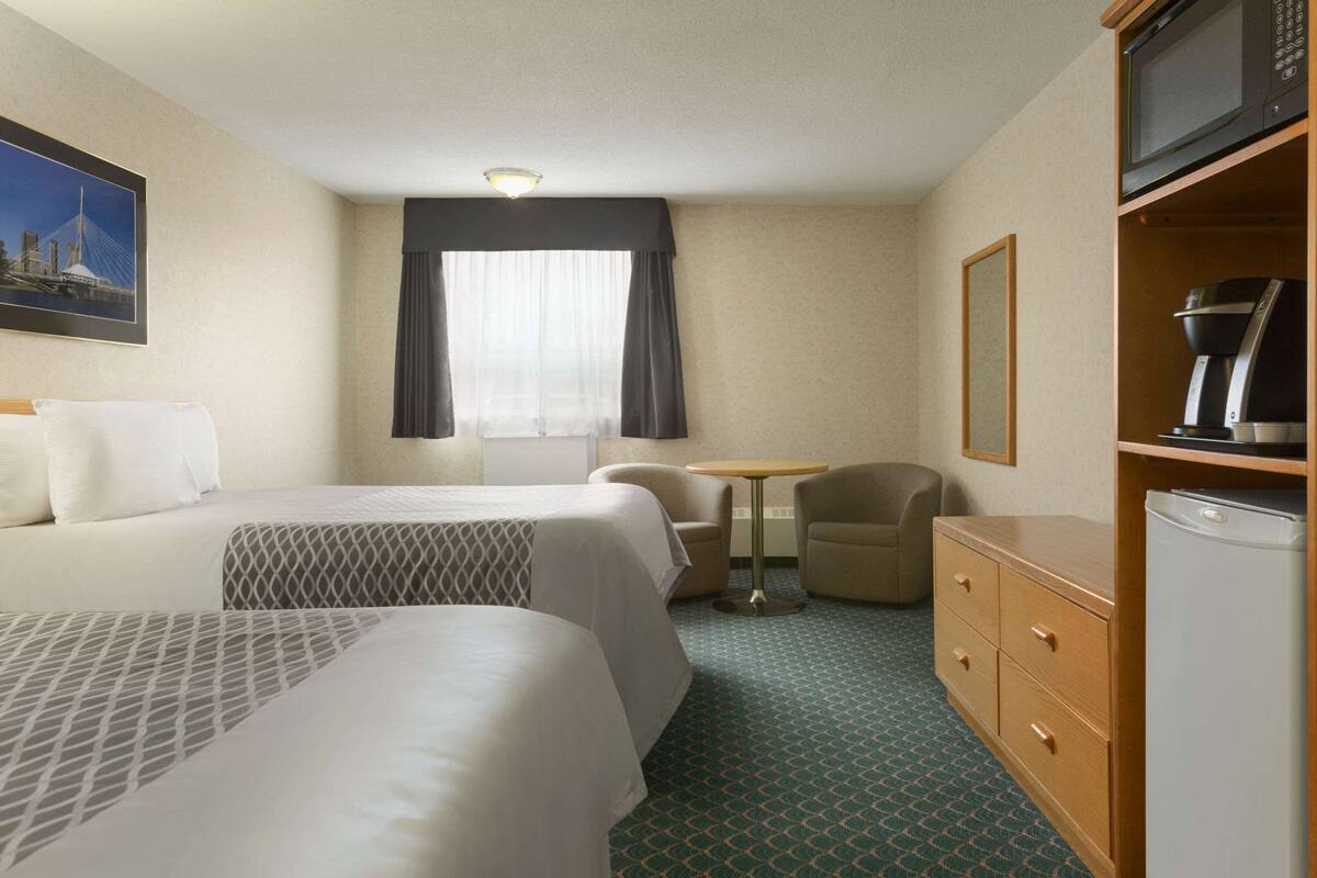 A hotel room with two beds, a small table, a chair, a microwave, a coffee maker, and a refrigerator.