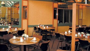 Un restaurante con mesas y sillas redondas, un techo alto con plantas colgantes y un espejo grande en una pared.