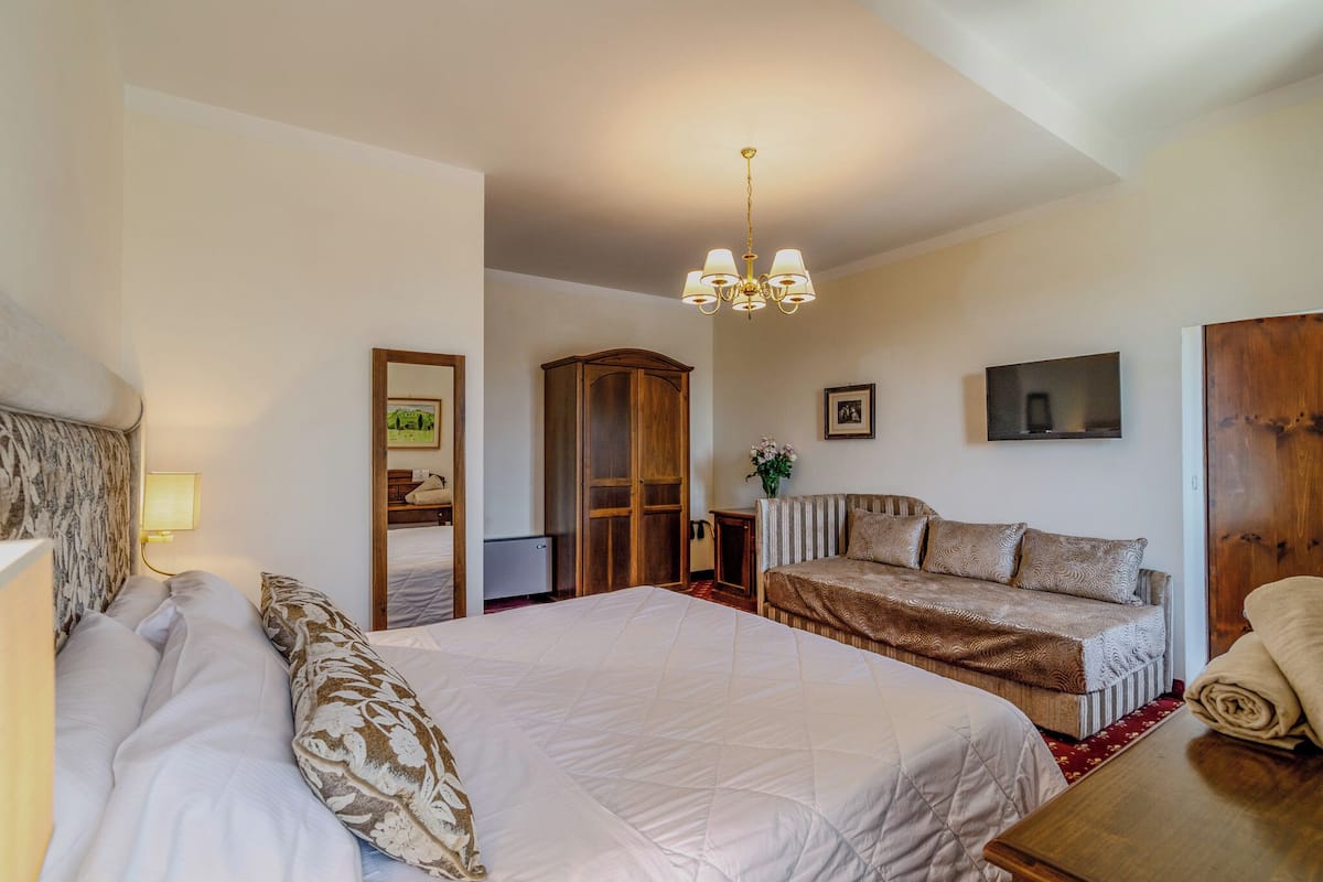 Ein Hotelzimmer mit einem großen Bett, einer Couch, einem Holzschrank, einem Fernseher und einer Kandelaber.
