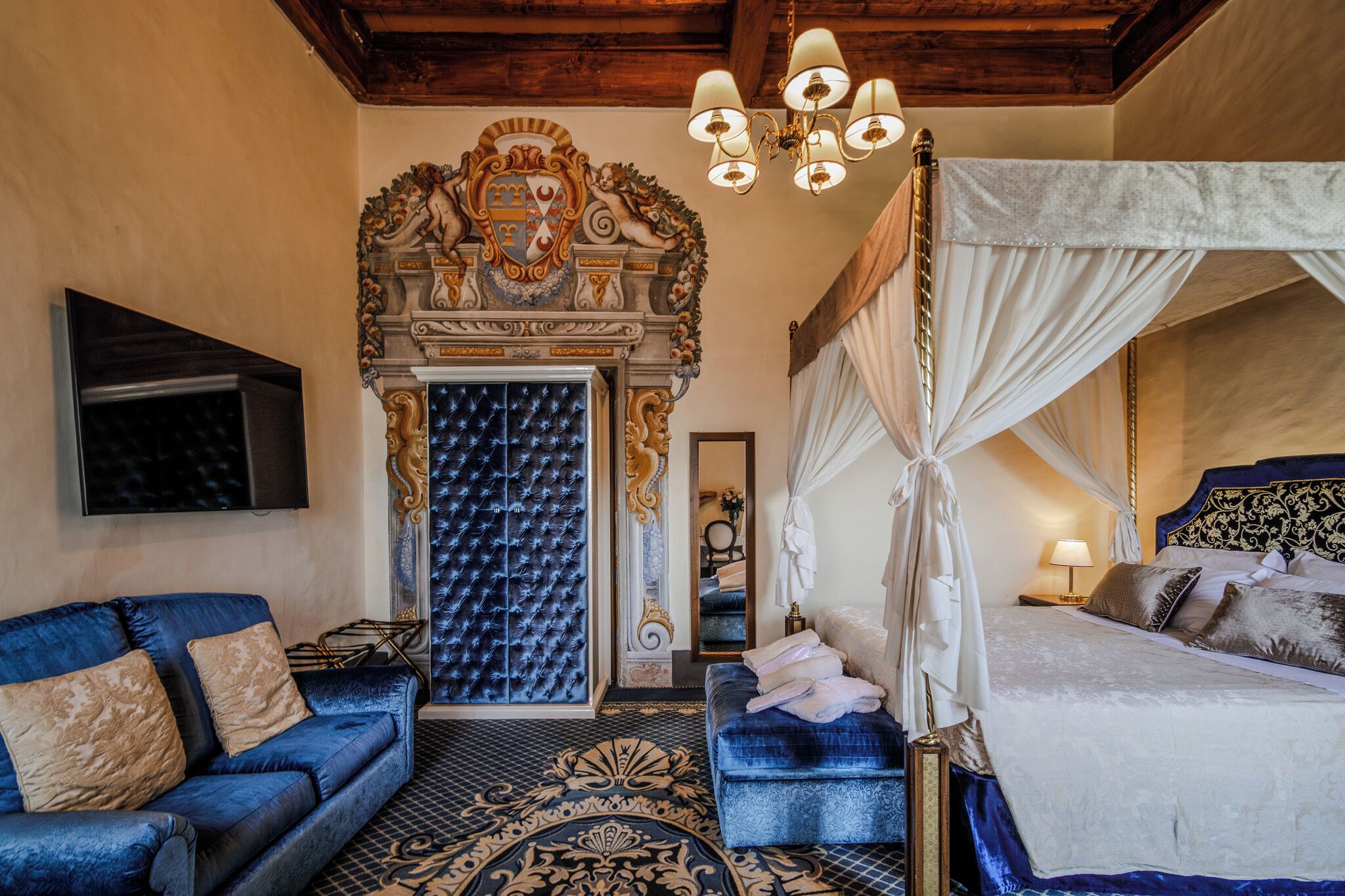 Un dormitorio lujoso con una cama grande, un sofá azul, una chimenea decorativa y una araña.