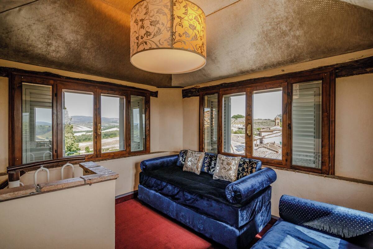 A room with a blue sofa, a red carpet, and a view of a distant landscape through large windows.
