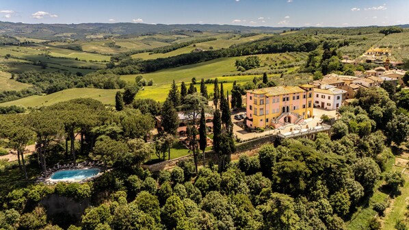 A large estate with a swimming pool, surrounded by lush greenery and hills.