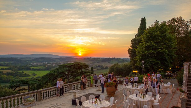 An outdoor dining area with round tables and chairs, set against a scenic backdrop of a sunset over rolling hills. - Villa Lecchi Hotel Wellness (Poggibonsi)