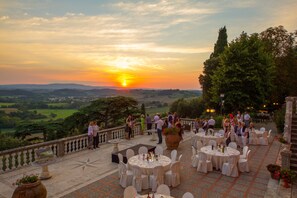 An outdoor dining area with round tables and chairs, set against a scenic backdrop of a sunset over rolling hills. - Villa Lecchi Hotel Wellness (Poggibonsi)