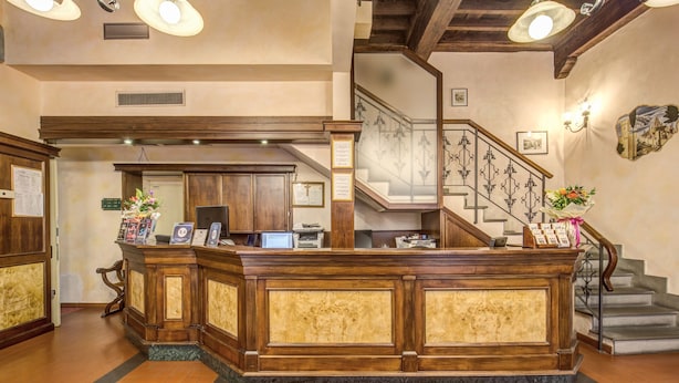 A reception desk with a wooden finish and marble inlays, a staircase with a wrought iron railing, and a patterned rug on the floor. - Residence La Repubblica (Florence)