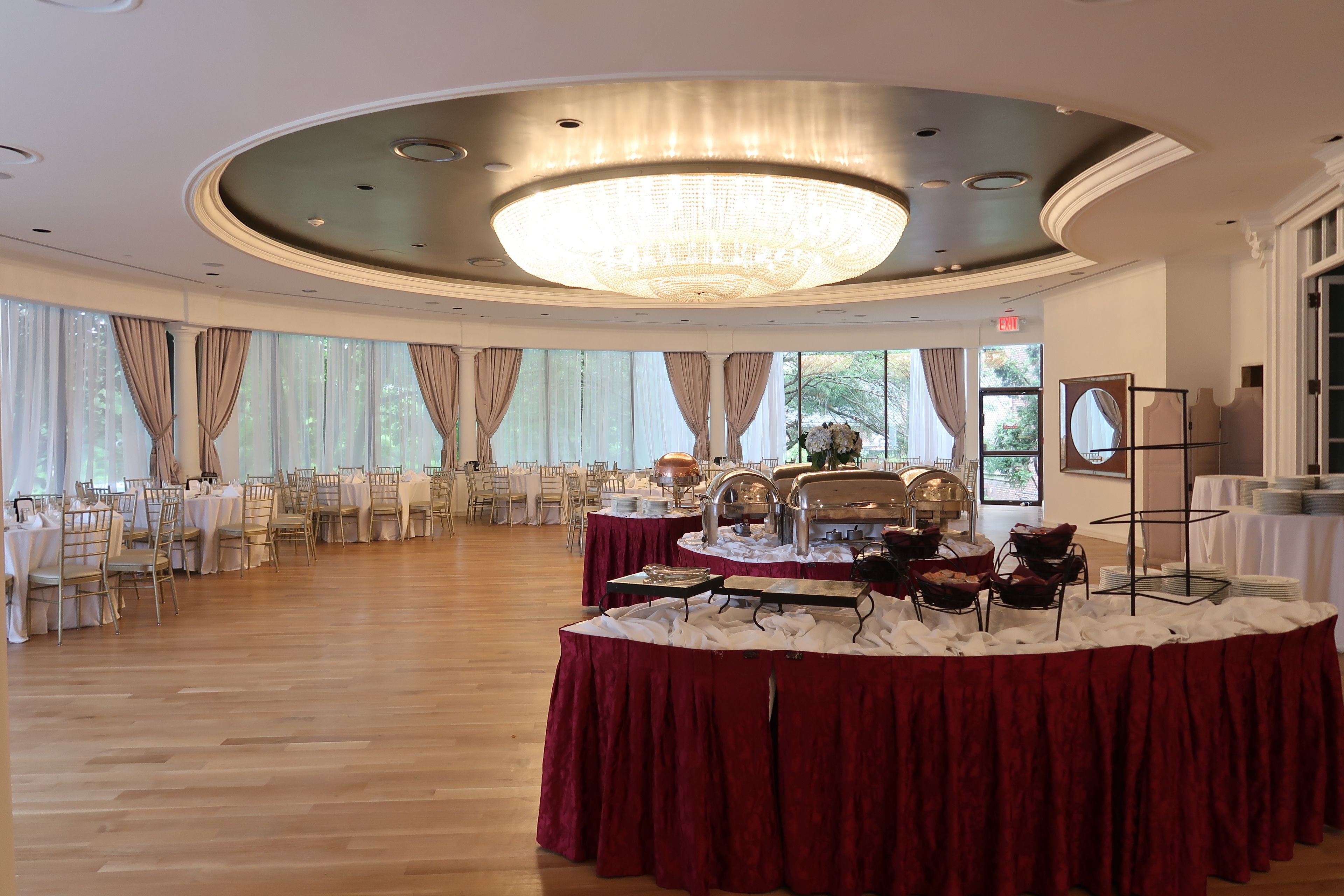 A banquet hall with round tables covered in red tablecloths, a large chandelier, and a buffet setup.