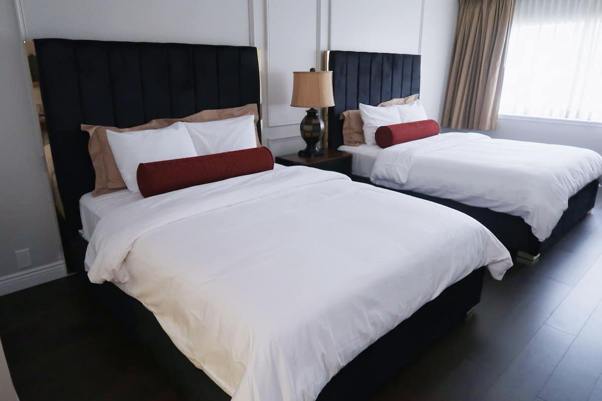 Dos camas dobles con sábanas blancas, cabeceros oscuros y almohadones rojos.