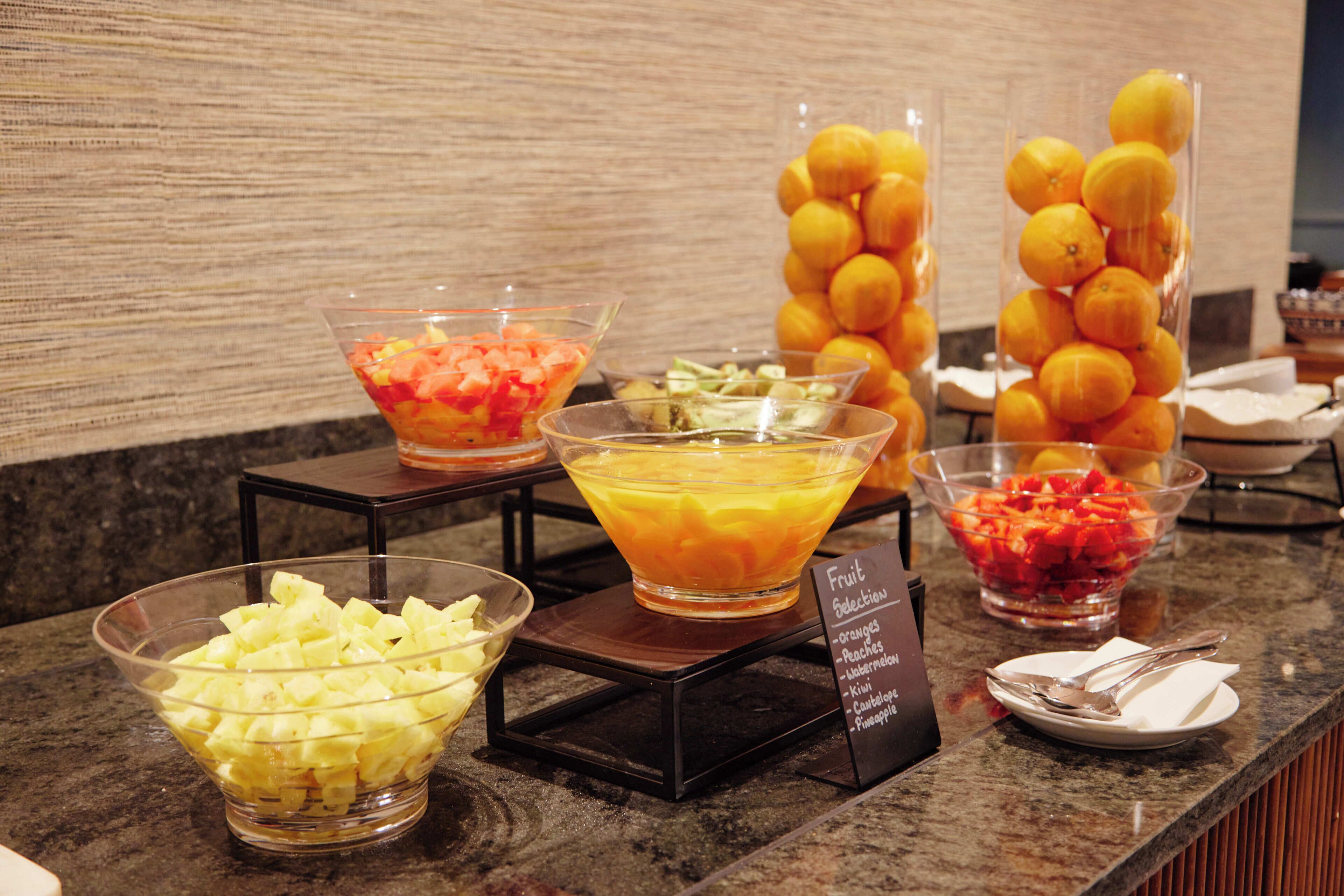 A buffet with various fruit selections including oranges, peaches, kiwi, watermelon, and pineapple.