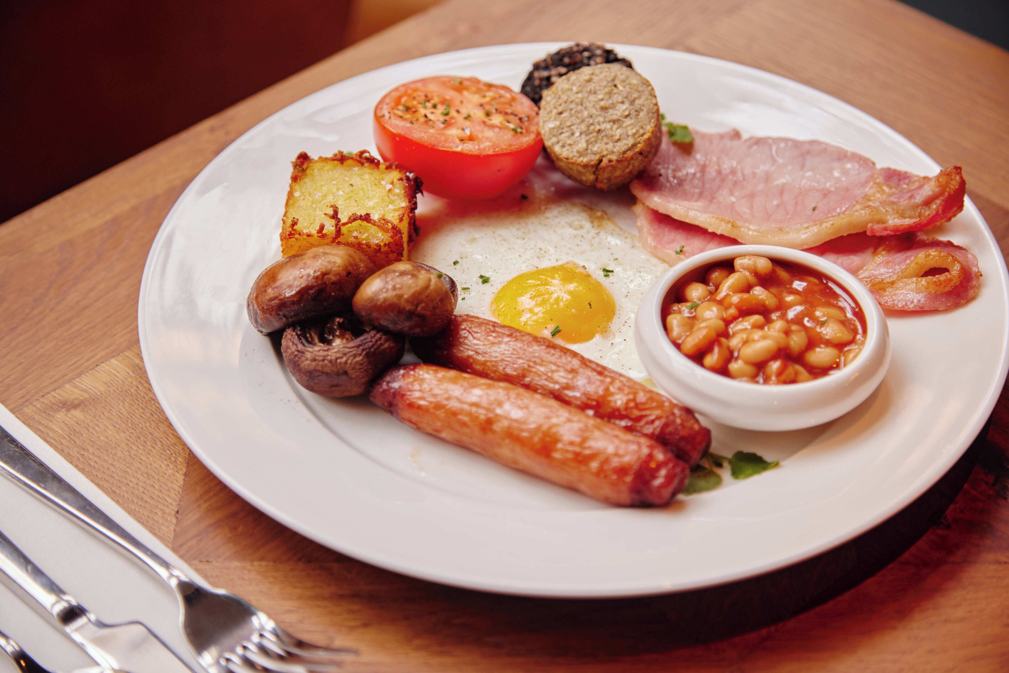 A plate of breakfast food including sausages, eggs, tomatoes, beans, and bacon.