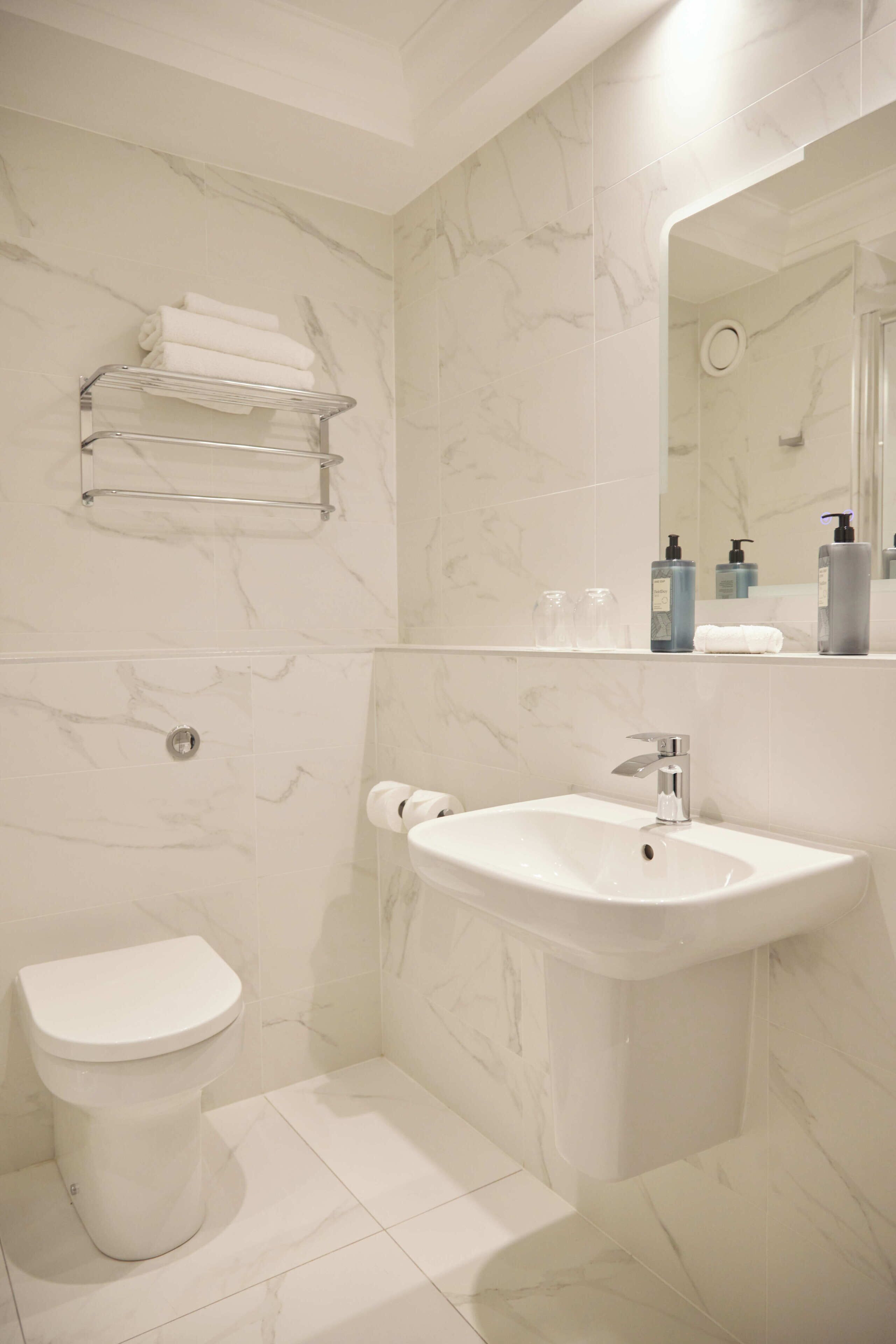 Un baño con inodoro, lavamanos, azulejos de mármol y un perchero para toallas.