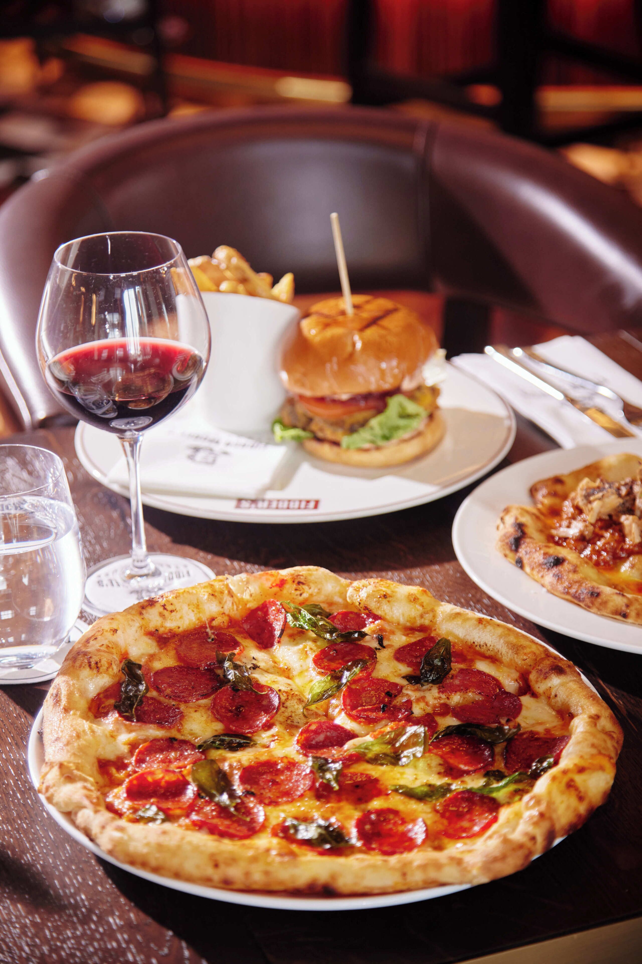 A dining table with a pizza, a glass of red wine, a burger, and a plate of fries.