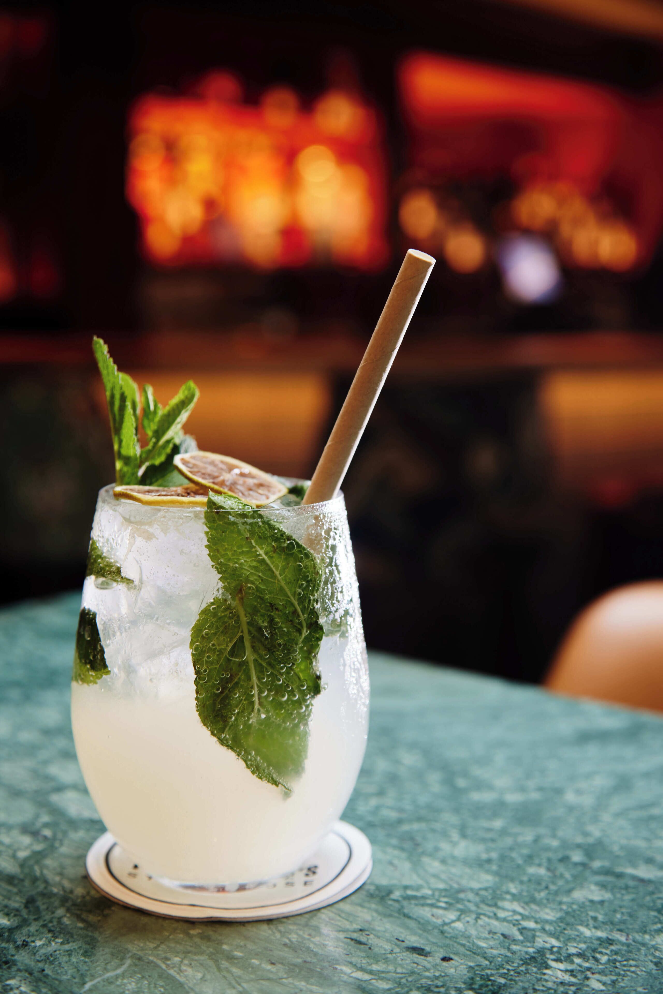 A glass of a clear beverage with mint leaves and a straw, placed on a coaster.