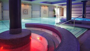 Een moderne binnenzwembadruimte met een centraal gelegen whirlpool, betegelde wanden en een trap naar een hoger niveau.