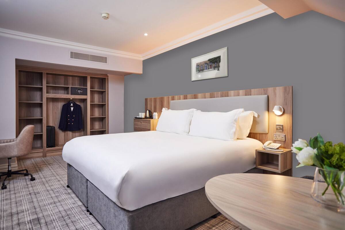 Habitación de hotel con una cama grande, un escritorio, una silla, un armario y una mesita de noche con un teléfono.