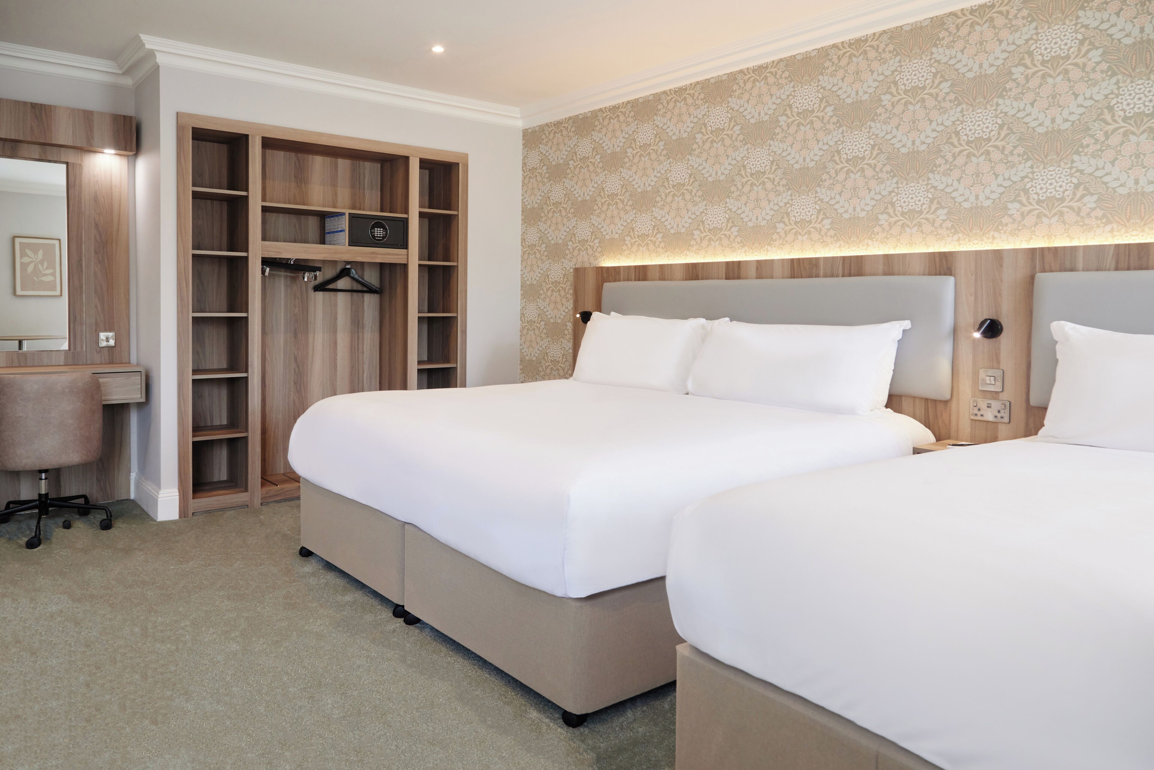 Habitación de hotel con dos camas, armario, escritorio y pared con diseño.