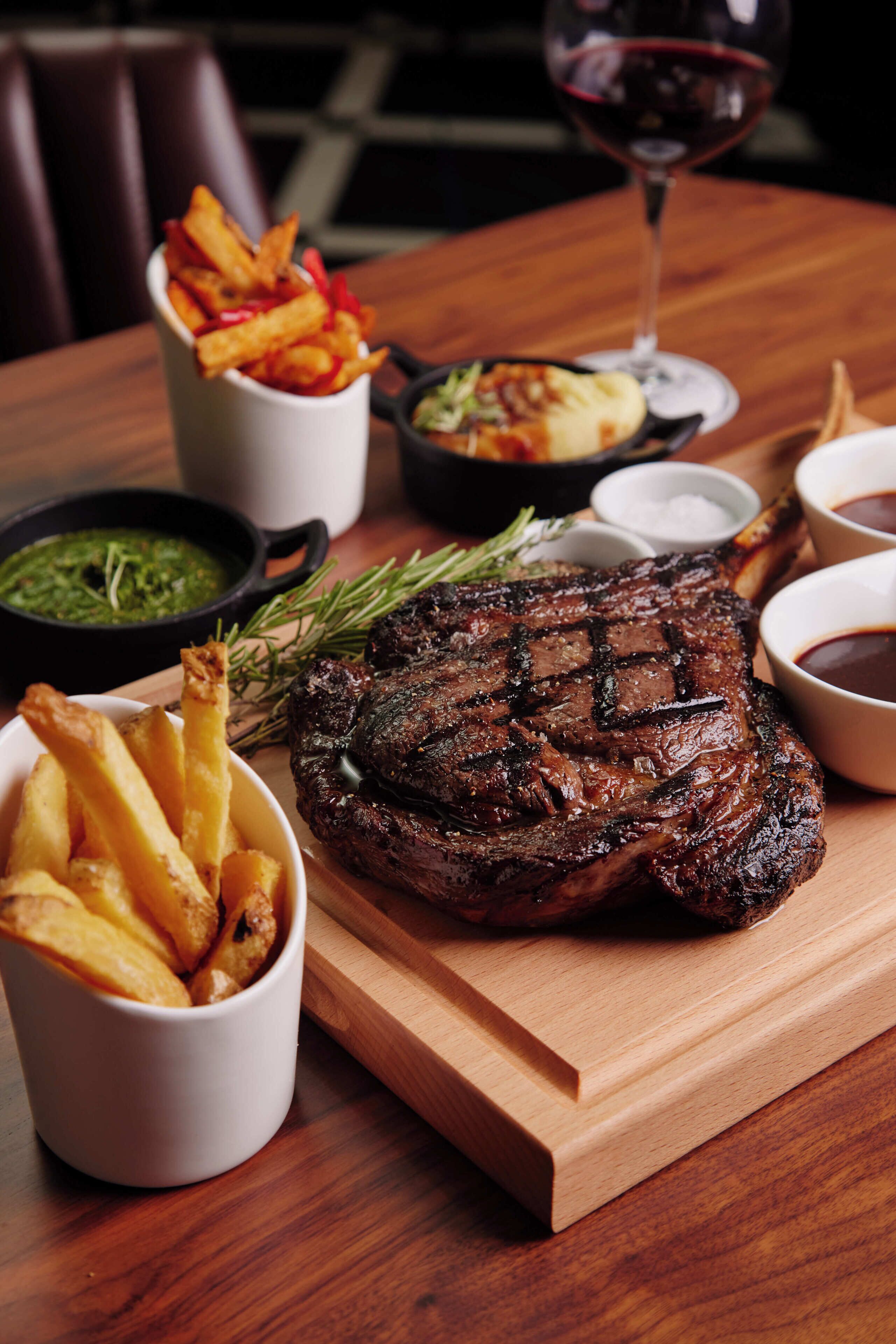 A steak with fries and sauces on a wooden board.