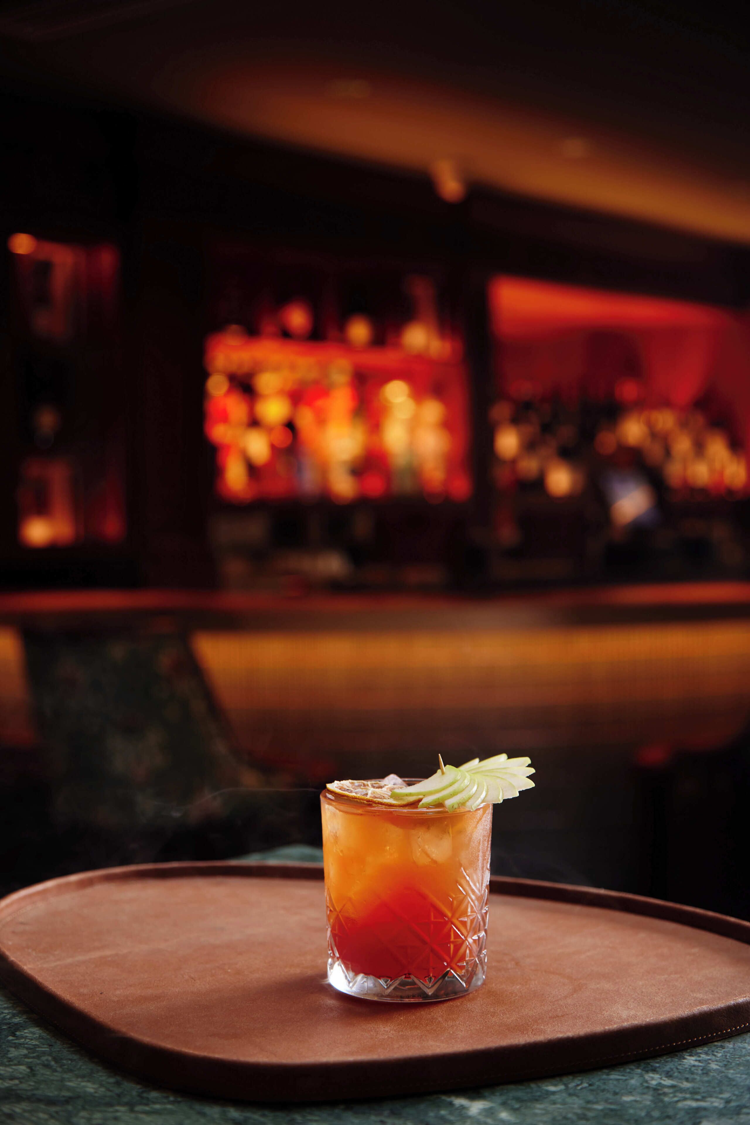 A cocktail on a tray with a blurred bar in the background.