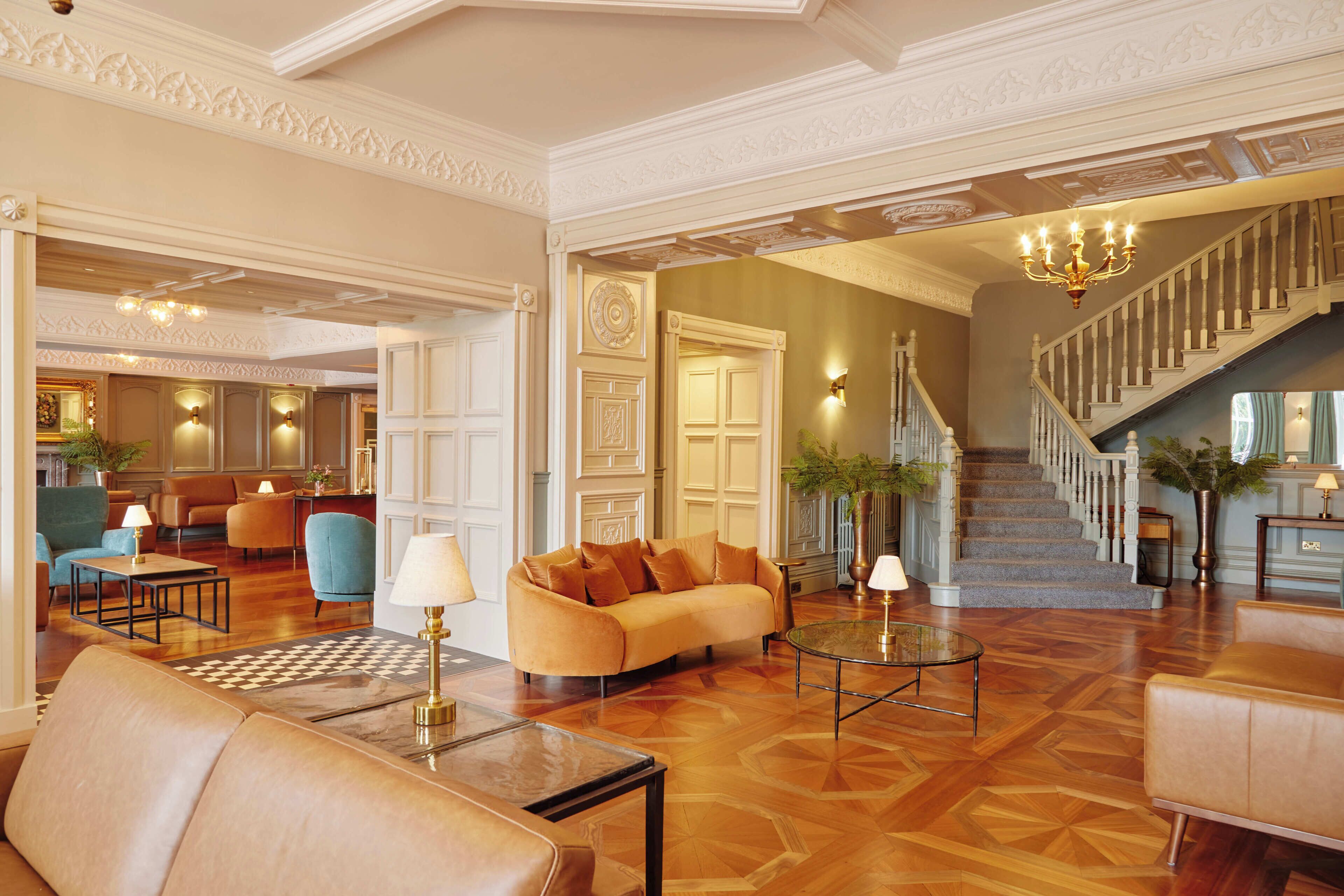 A spacious lobby with a grand staircase, plush seating, and a chandelier.