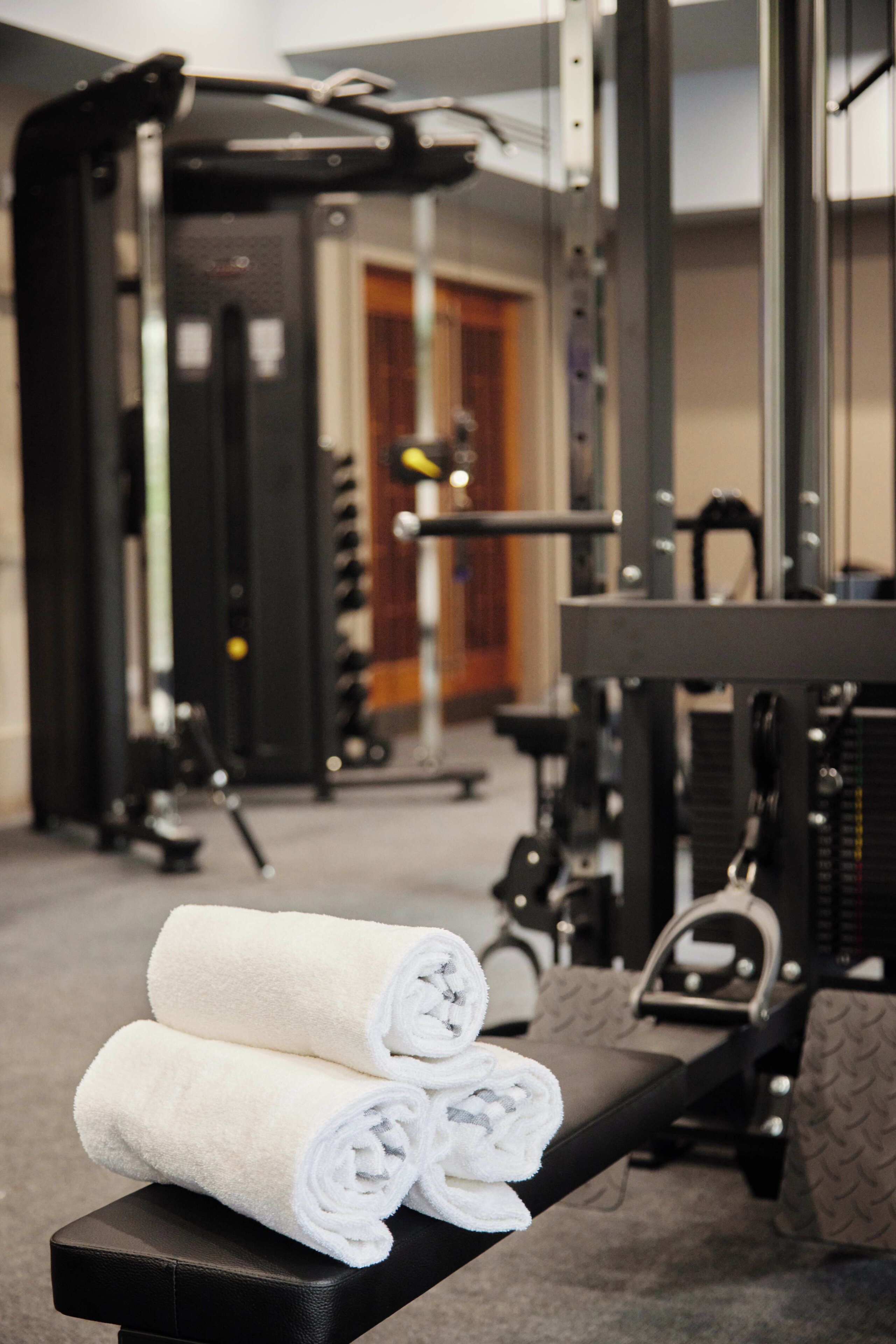 A gym with exercise equipment, a bench with towels, and a mirror.