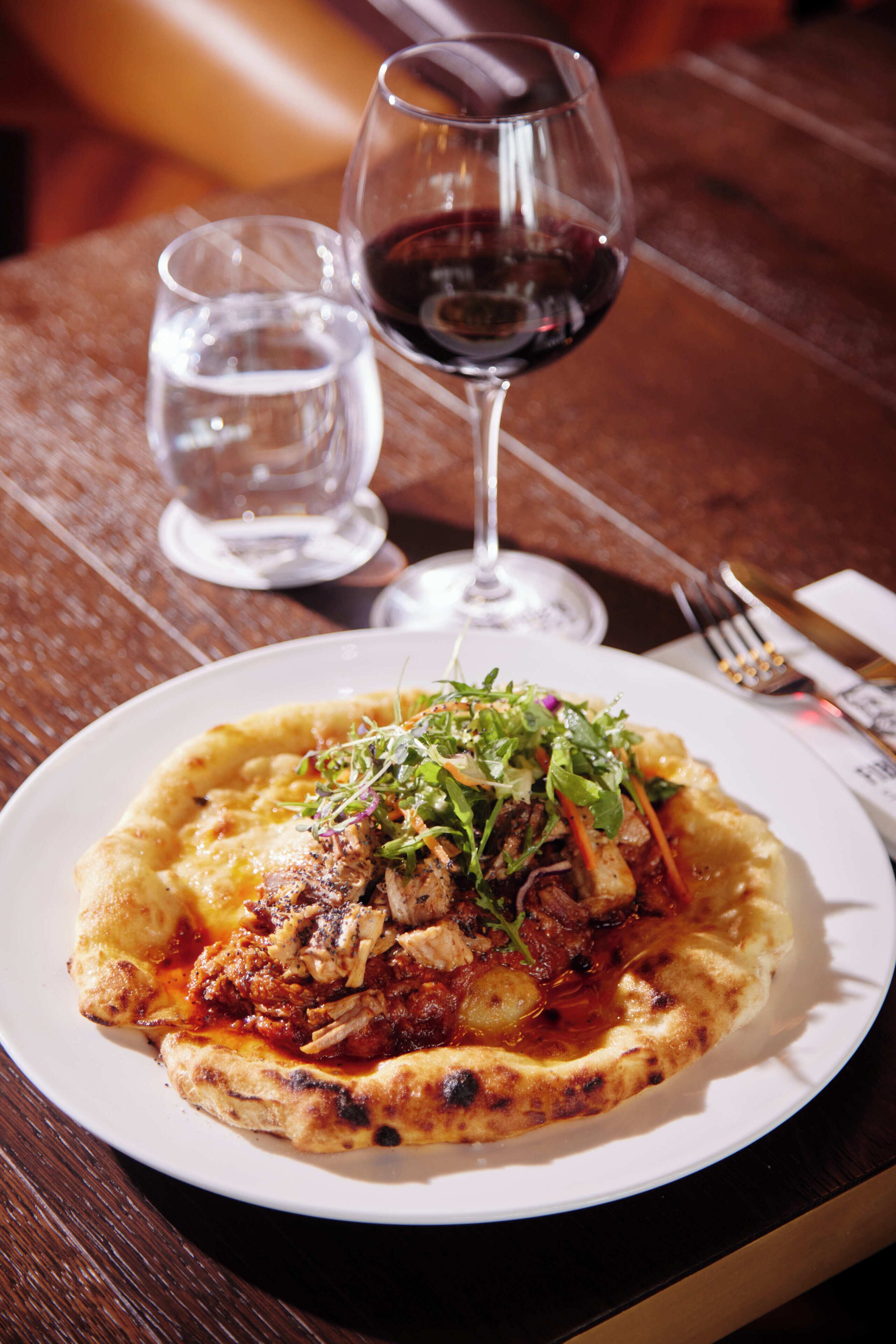 A plate of food with a glass of red wine and a glass of water on a wooden table.