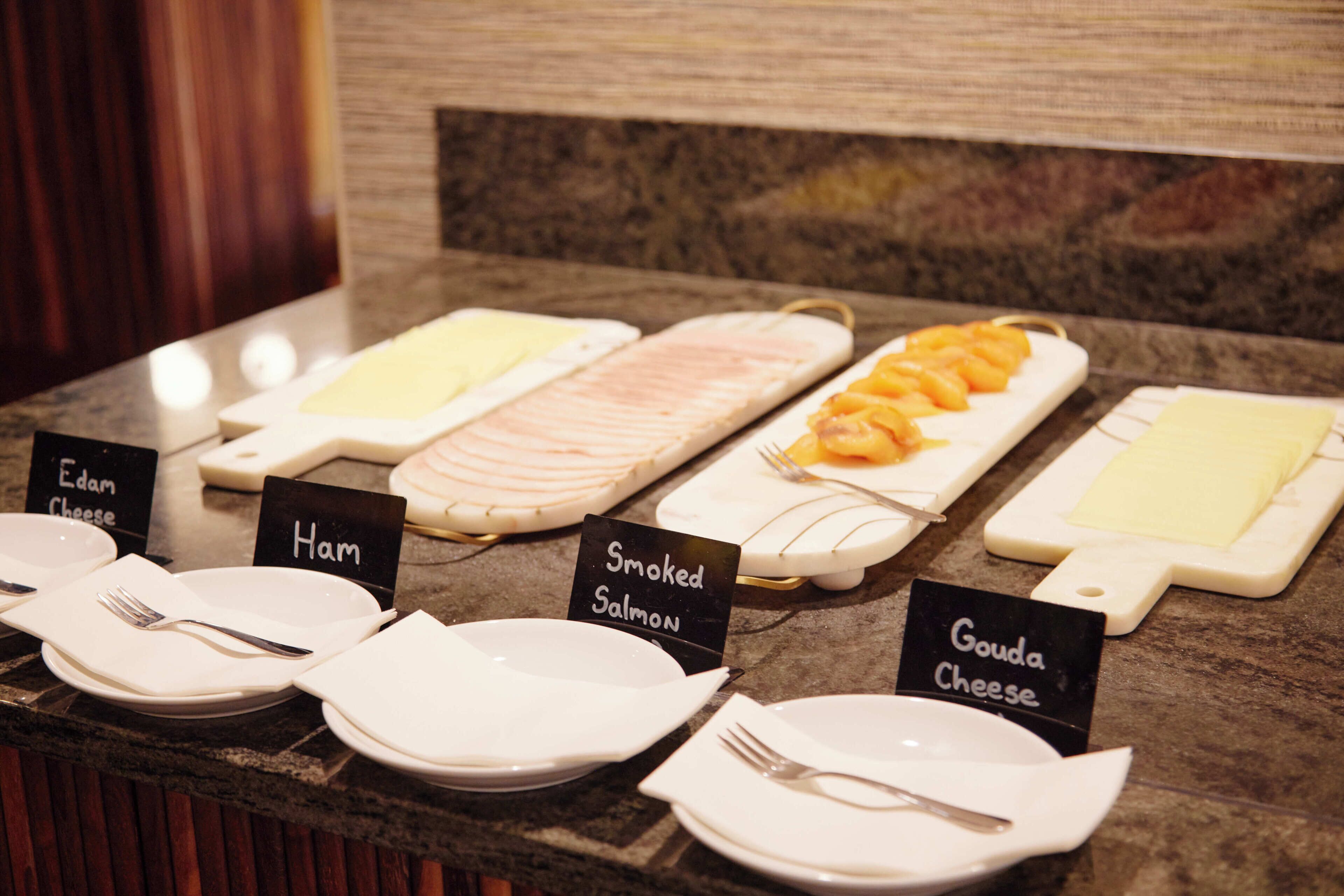 Un buffet con piatti etichettati per salmone affumicato, formaggio gouda e formaggio edam.