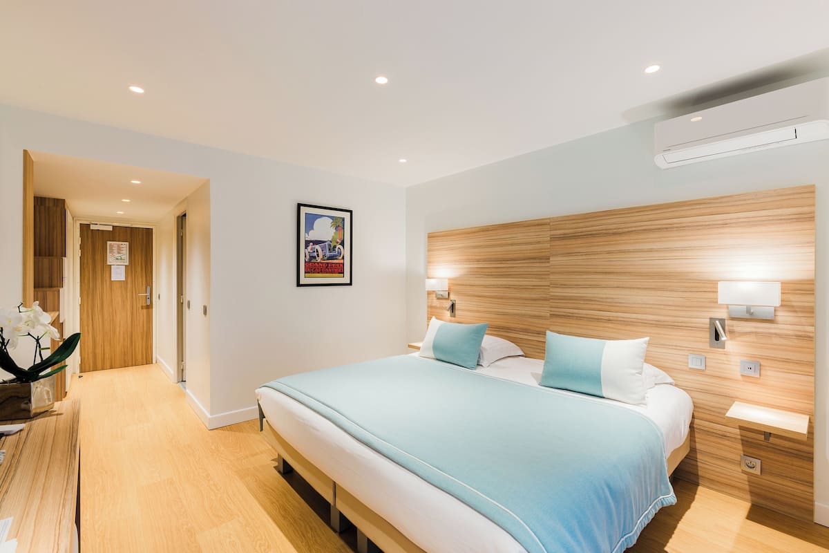 A hotel room with a large bed, wooden headboard, bedside tables, and an air conditioning unit.