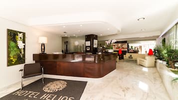 A hotel reception area with a marble floor, a reception desk, a sofa, and a large floral painting on the wall.