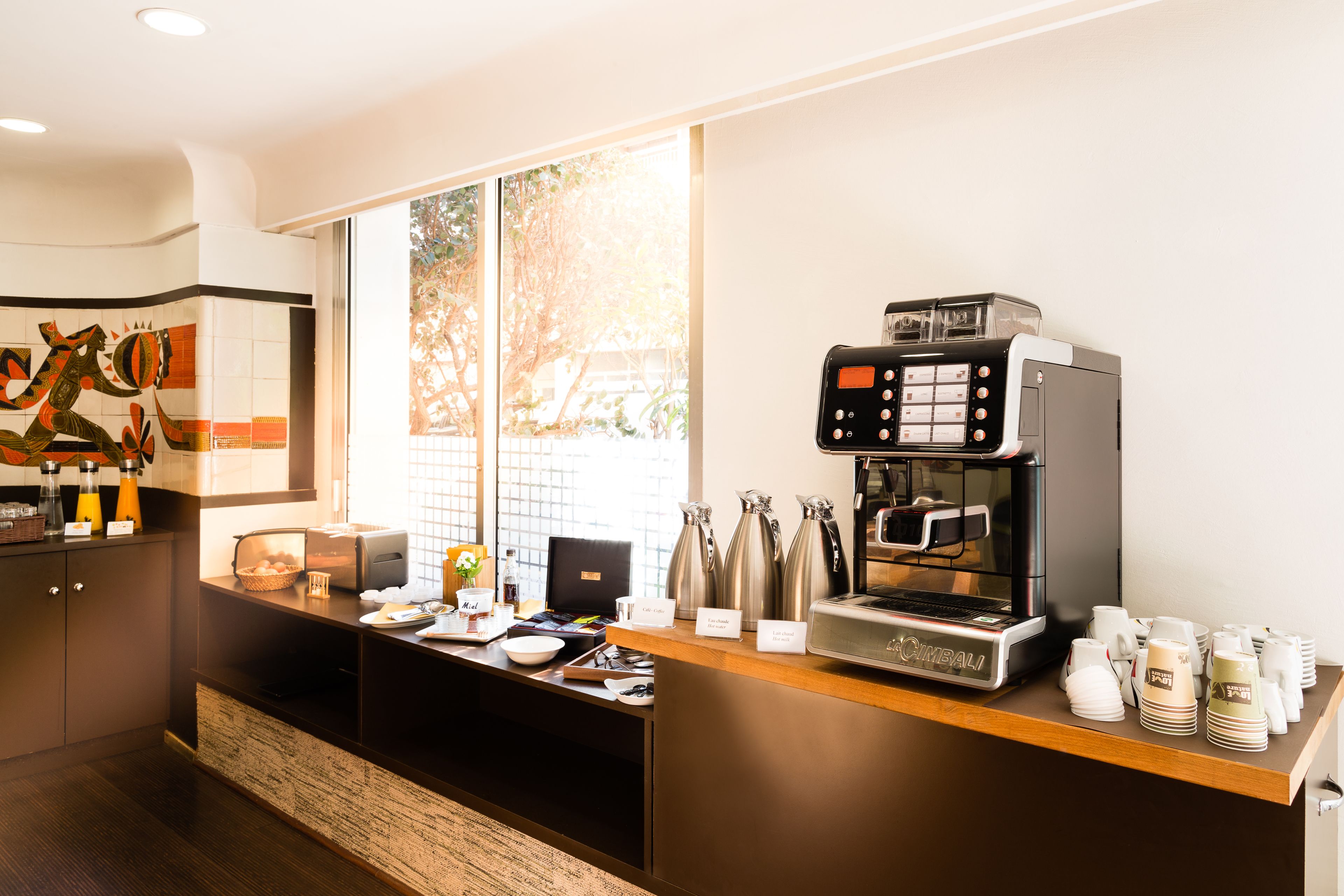 A modern coffee station with a coffee machine, cups, and a menu board.