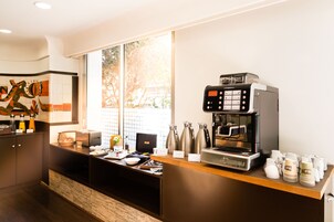 A modern coffee station with a coffee machine, cups, and a menu board.