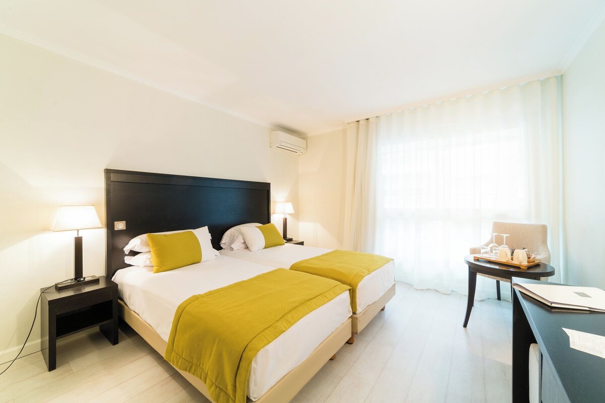 Habitación de hotel con dos camas, un escritorio y una lámpara.