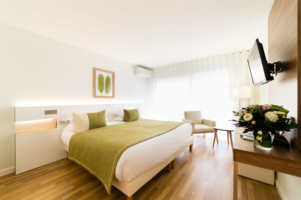 A hotel room with a bed, a desk, a chair, a TV, and a window with curtains.