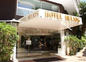 A hotel entrance with a glass facade, a sign reading "HOTEL HELIOS," and a doormat with the hotel's name.