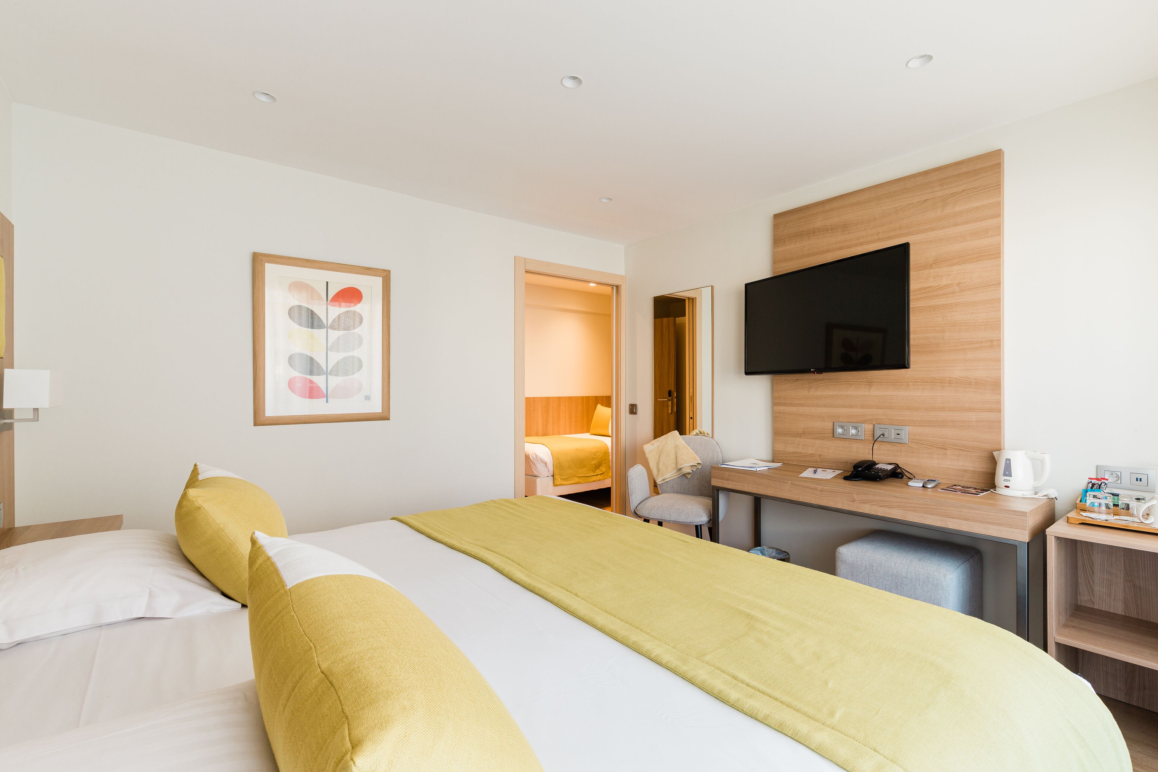 A hotel room with a bed, a desk, a chair, a television, and a bathroom visible through an open door.