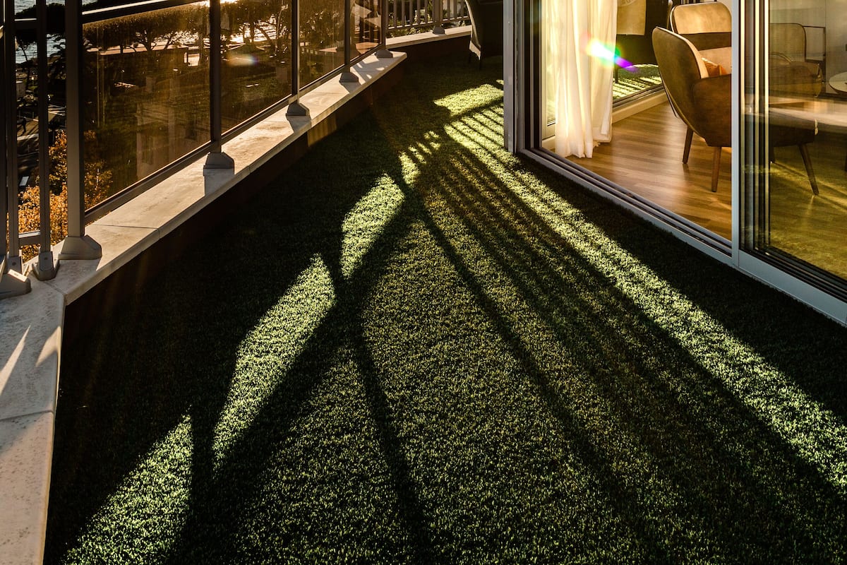 A balcony with a glass railing overlooking a body of water and a sunset.
