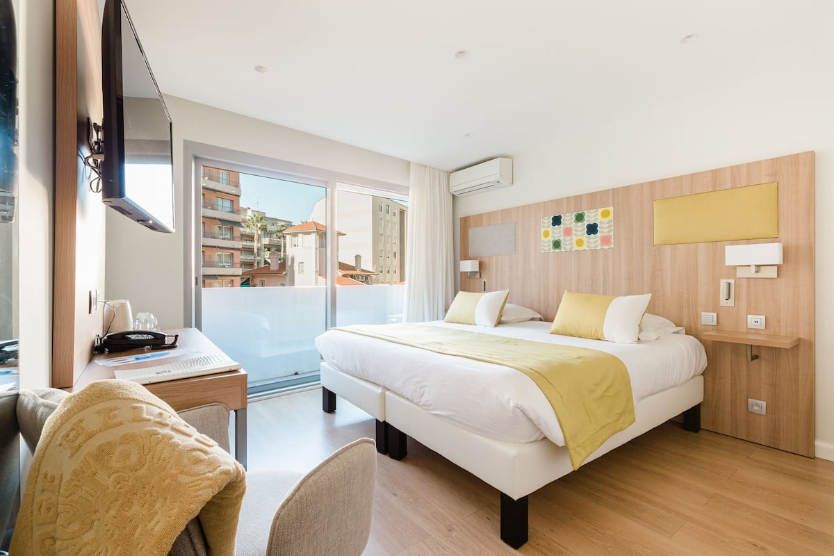 A hotel room with a bed, desk, chair, and a view of the outside.