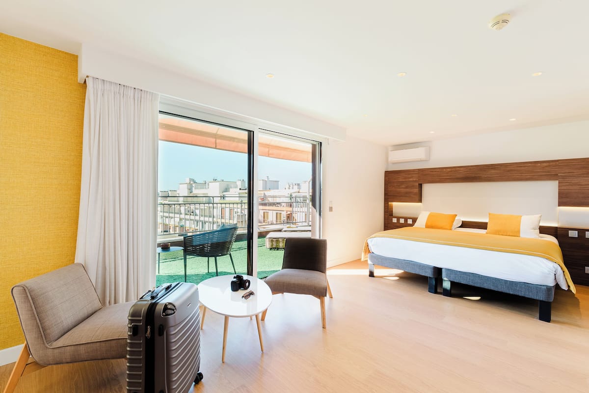 A hotel room with a bed, a chair, a table, and a suitcase.